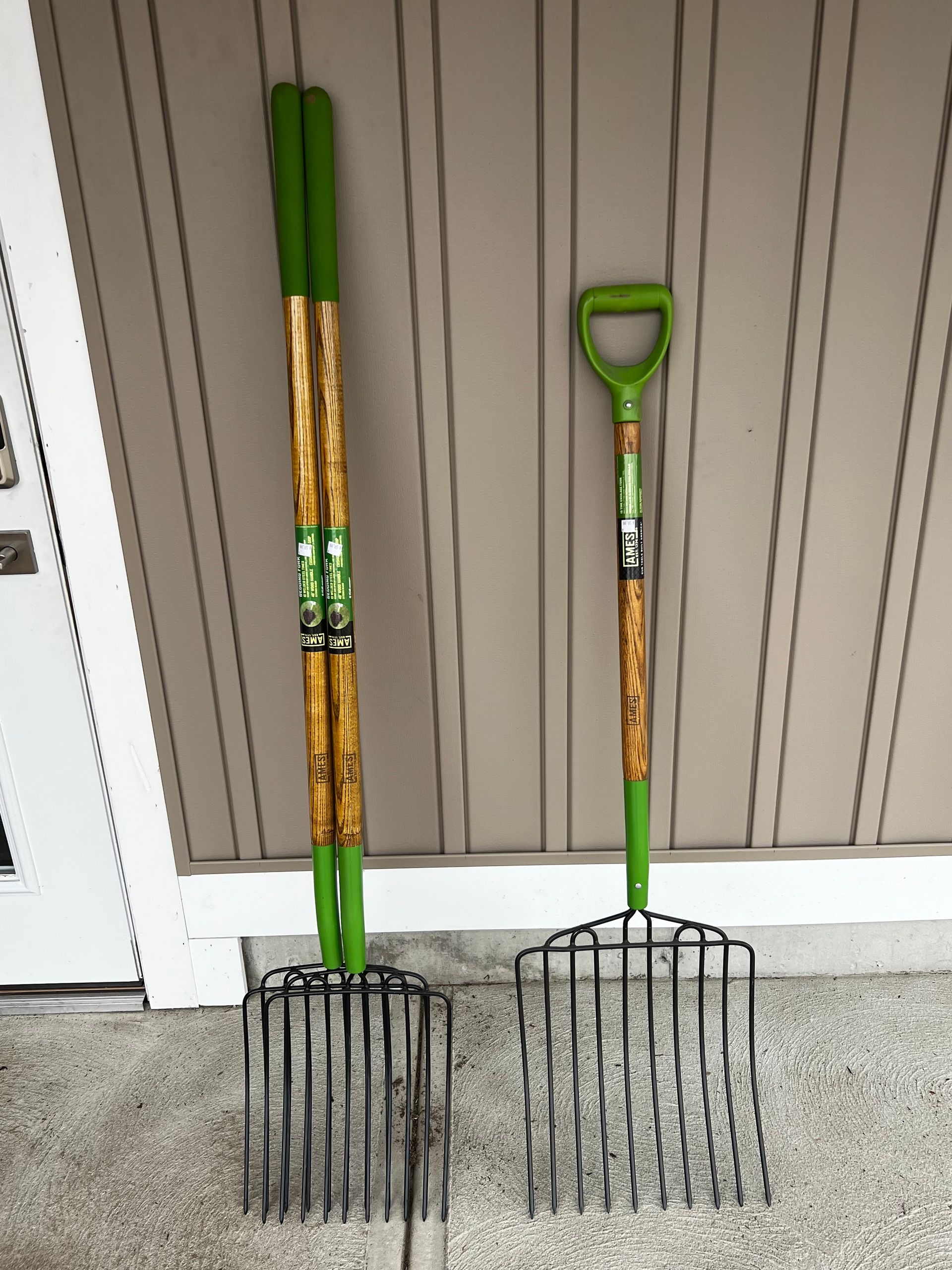 Two forks with green handles are sitting on the ground in front of a wall.
