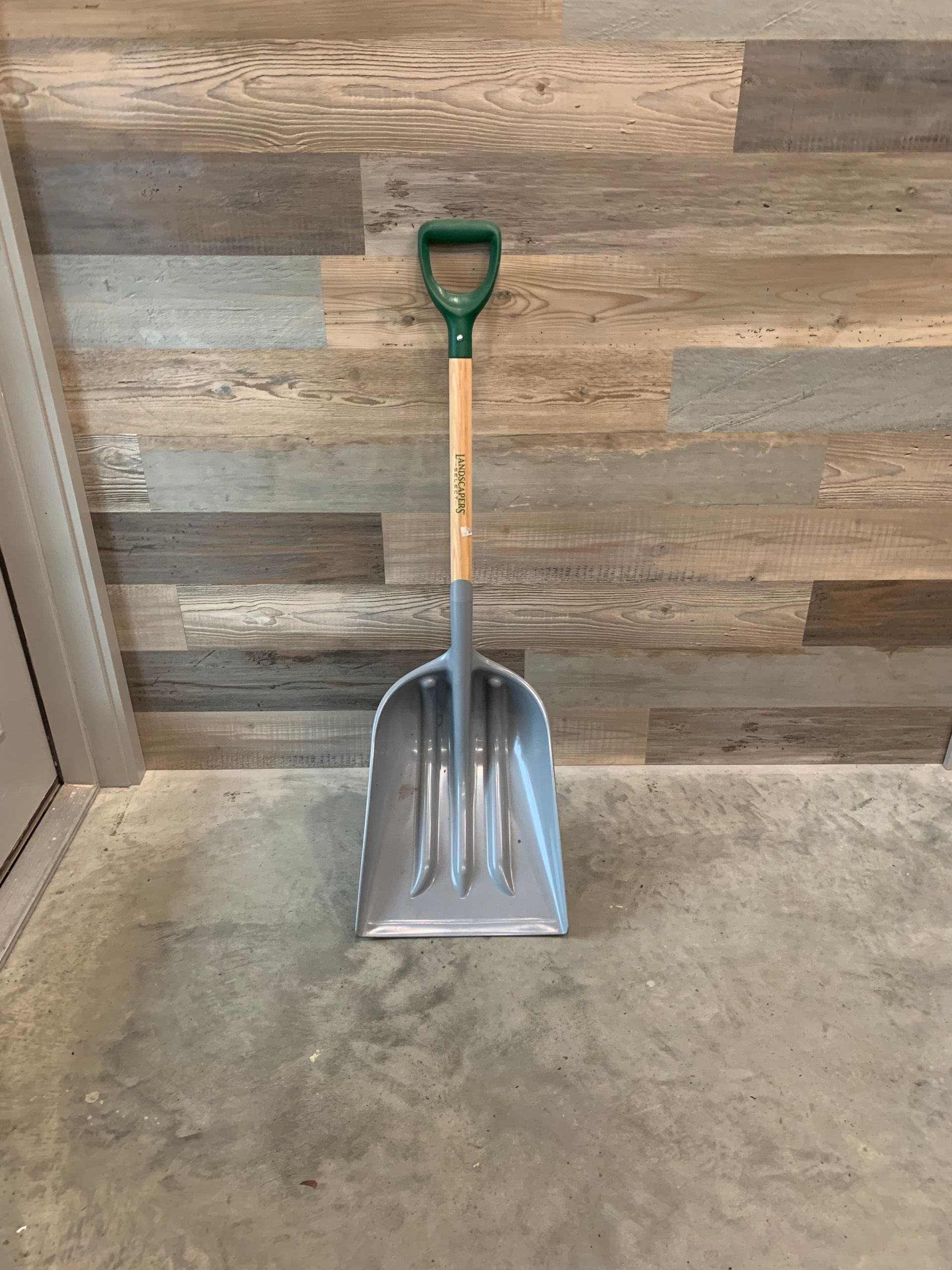 A shovel with a green handle is sitting on a concrete floor.