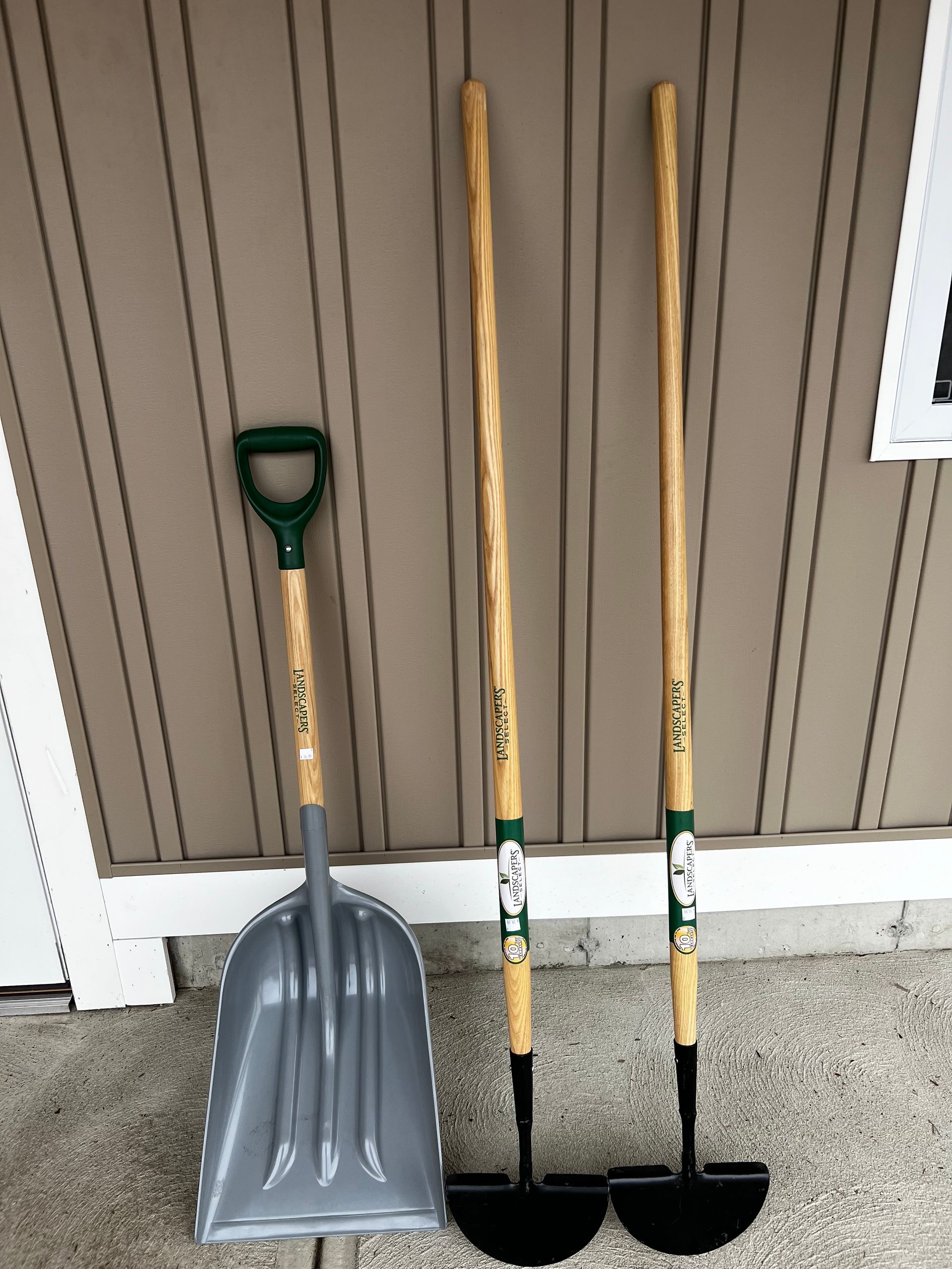 A shovel , hoe , and pitchfork are sitting in front of a building.