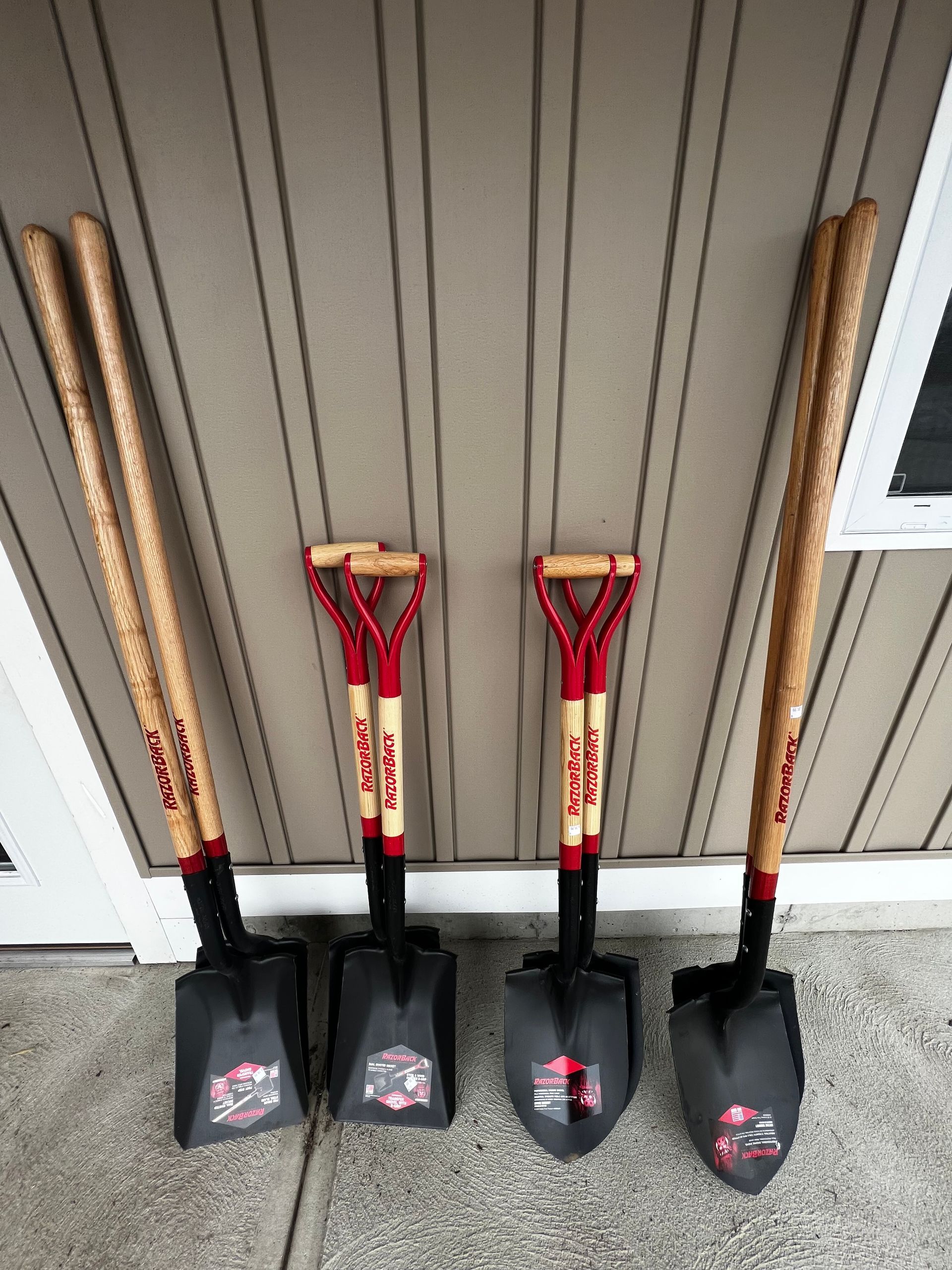 Four shovels with wooden handles are lined up against a wall.