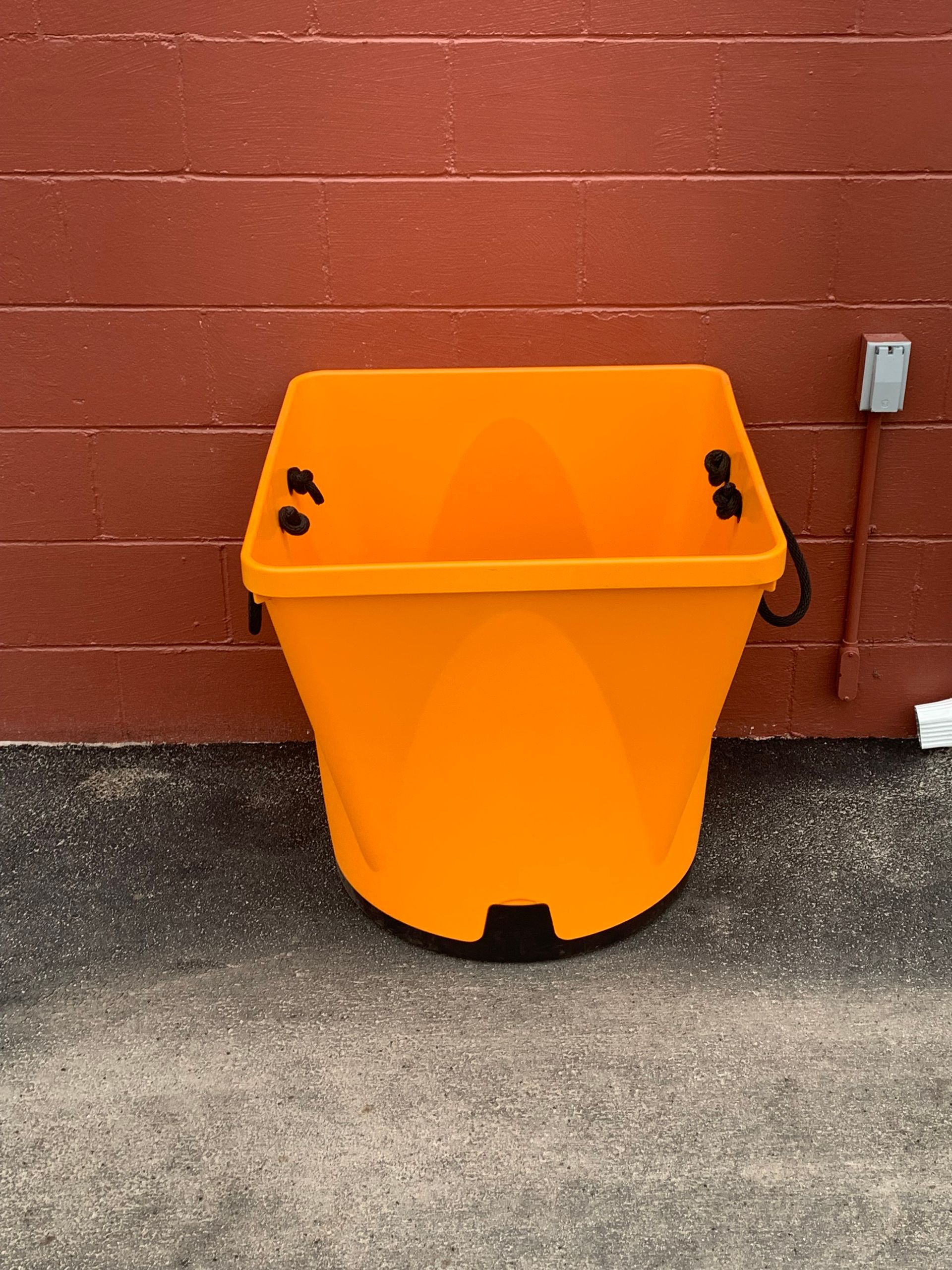 An orange trash can is sitting in front of a red brick wall.