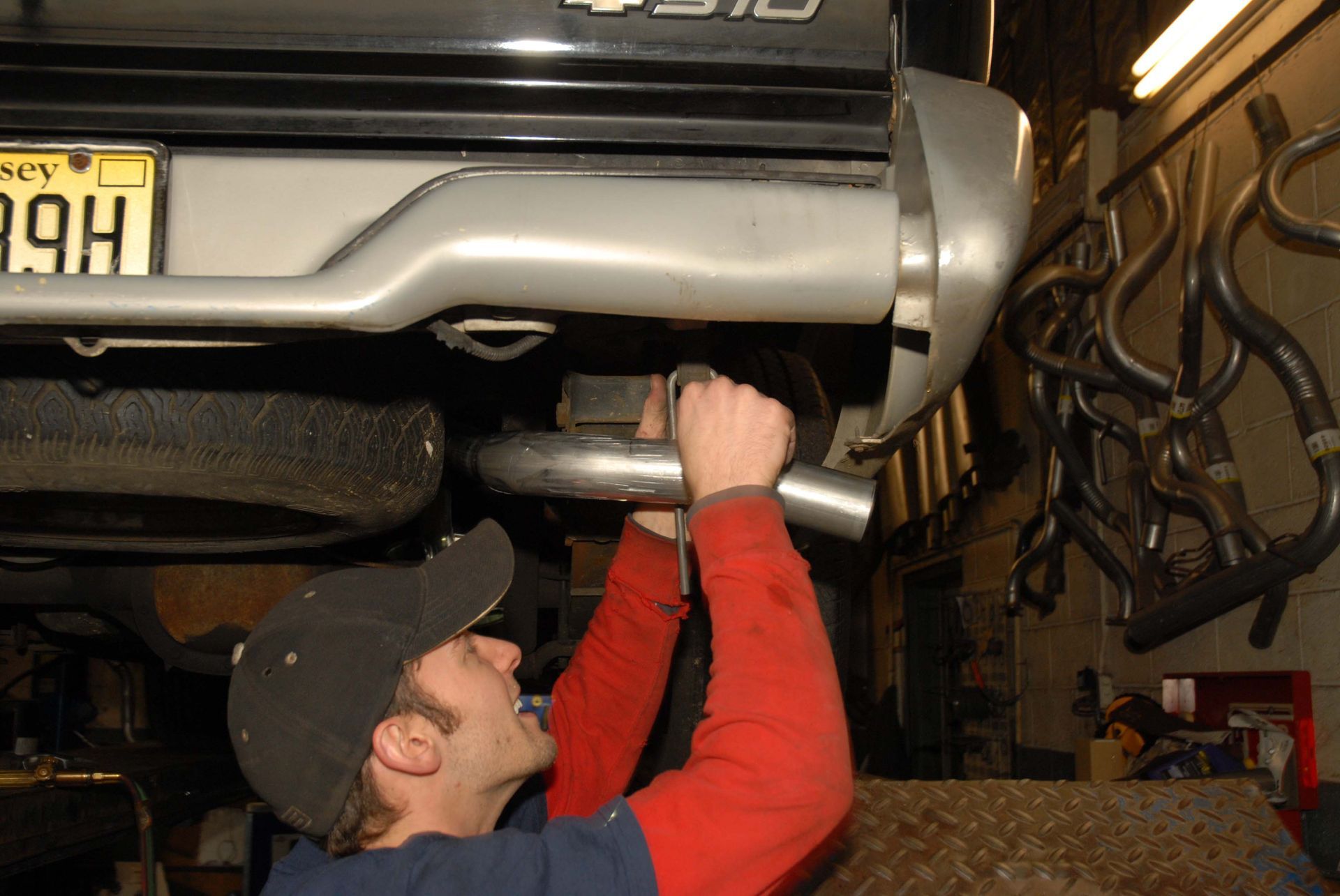 Man installing exhaust pipe under a truck bumper in a garage.