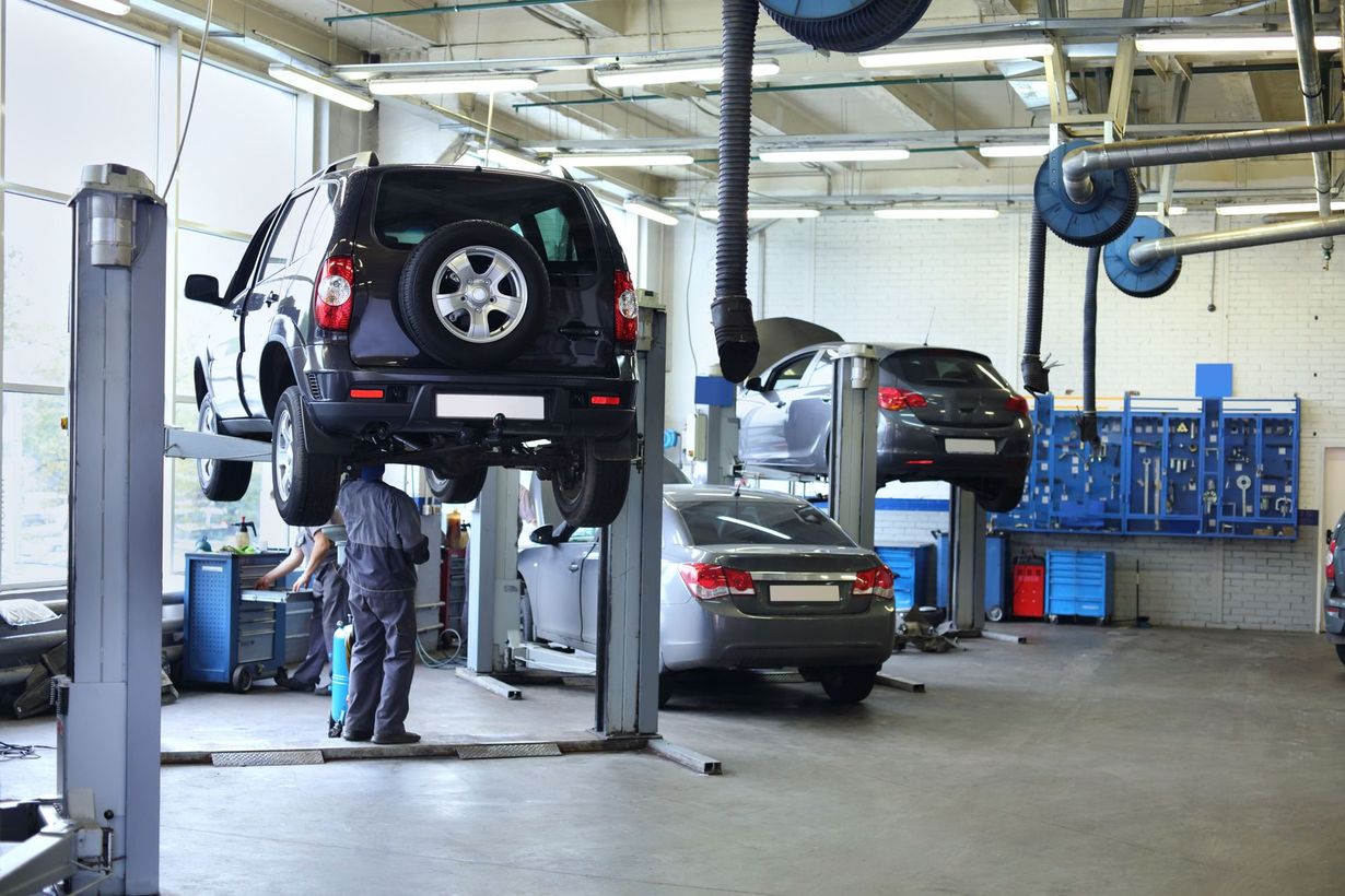 Cars on lifts in a mechanic's garage; a technician works on a car.