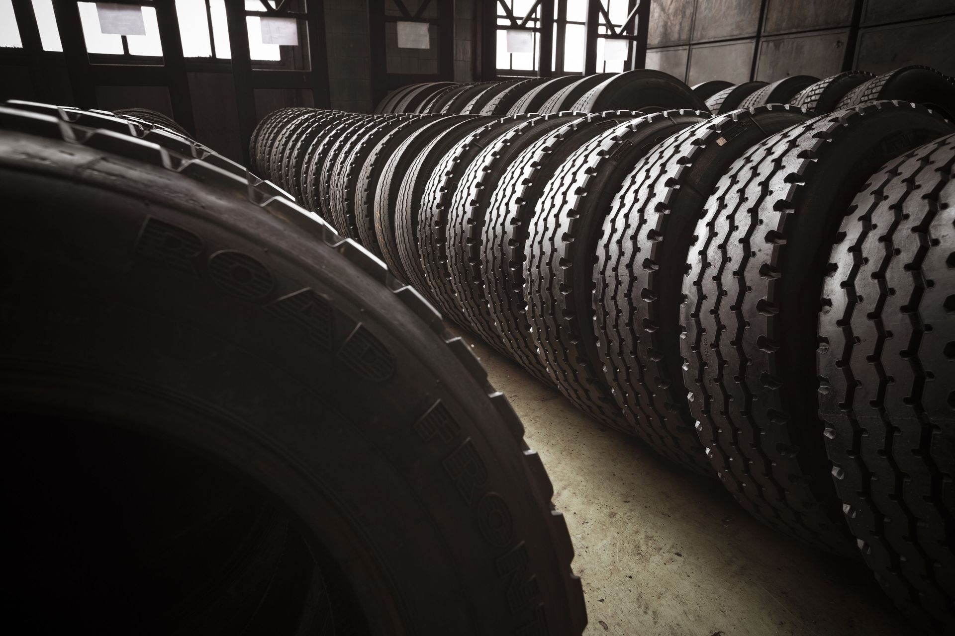 Rows of tires stacked in a warehouse, some in the foreground, with visible treads.