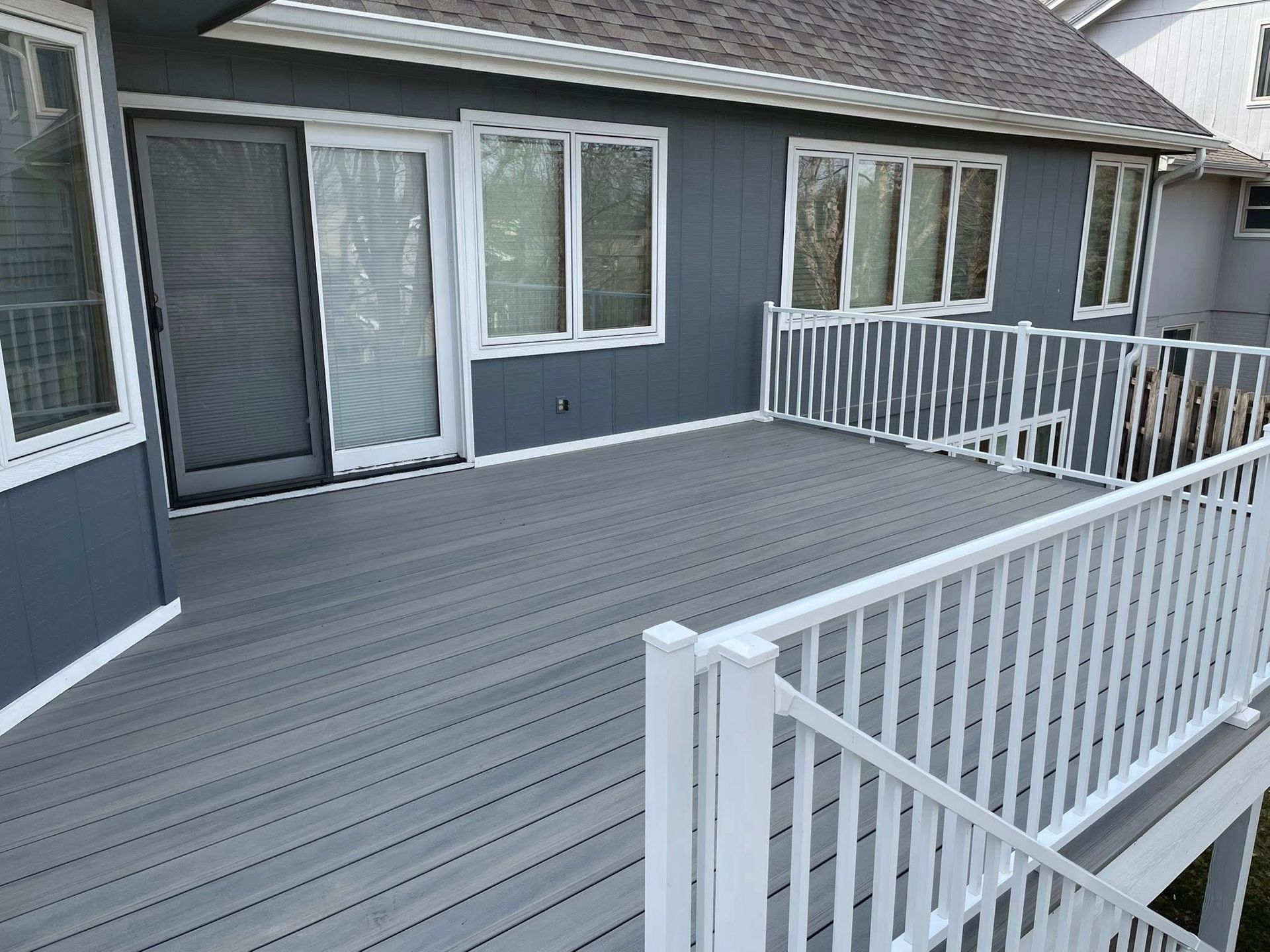 A gray deck with a white railing is sitting in front of a house.
