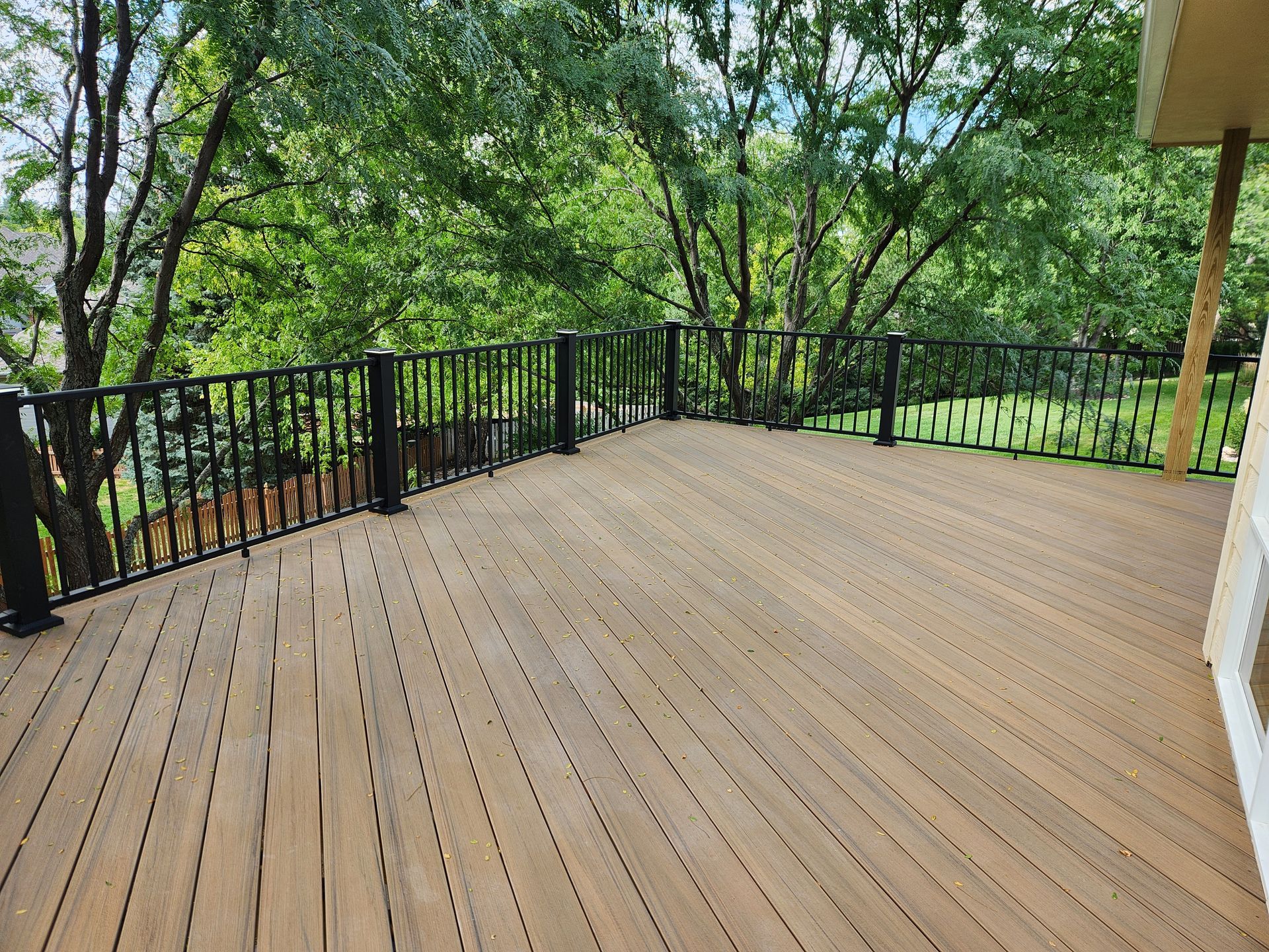 A large wooden deck with a black railing and trees in the background.