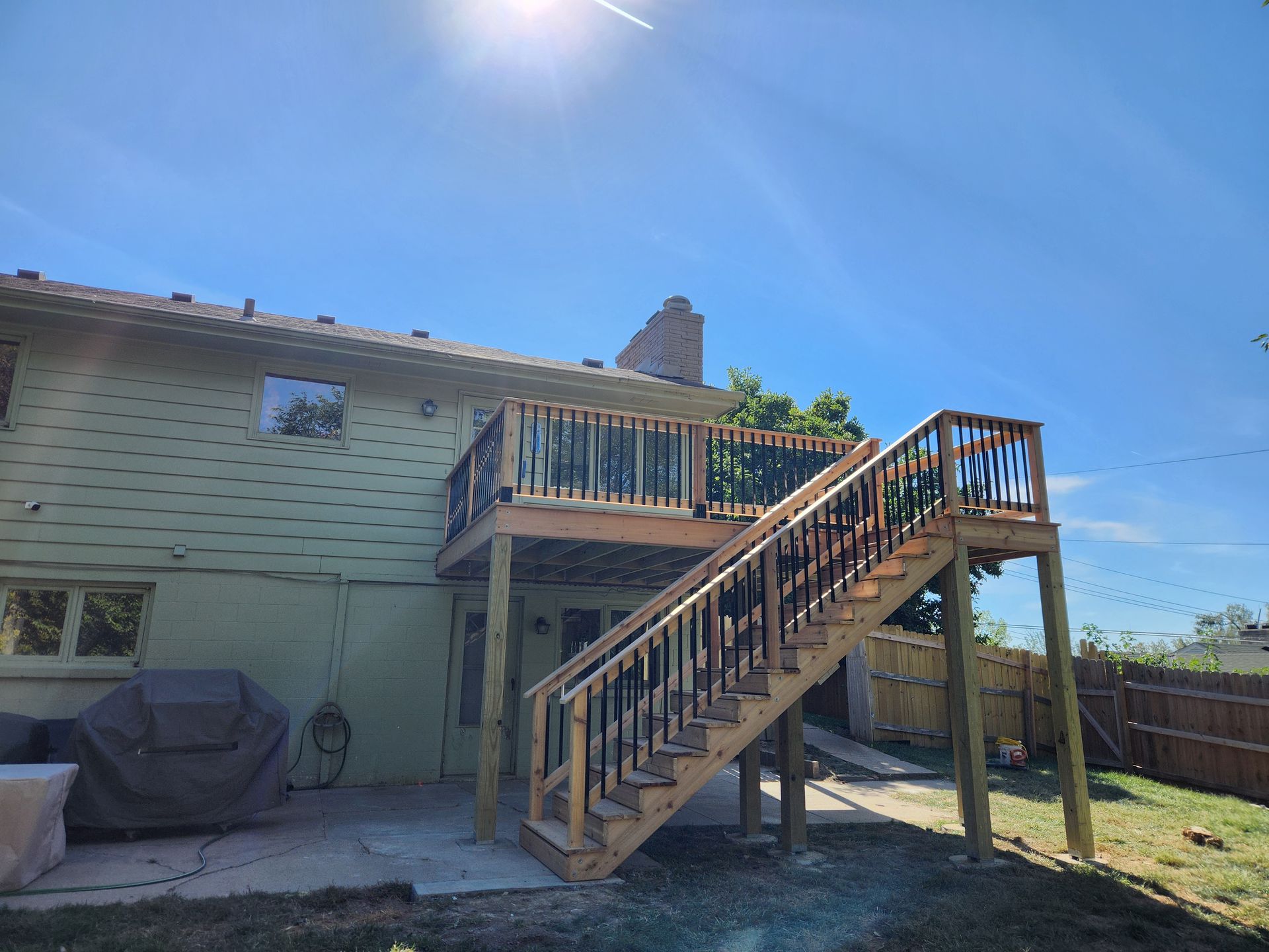 A wooden deck with stairs leading up to it is in the backyard of a house.