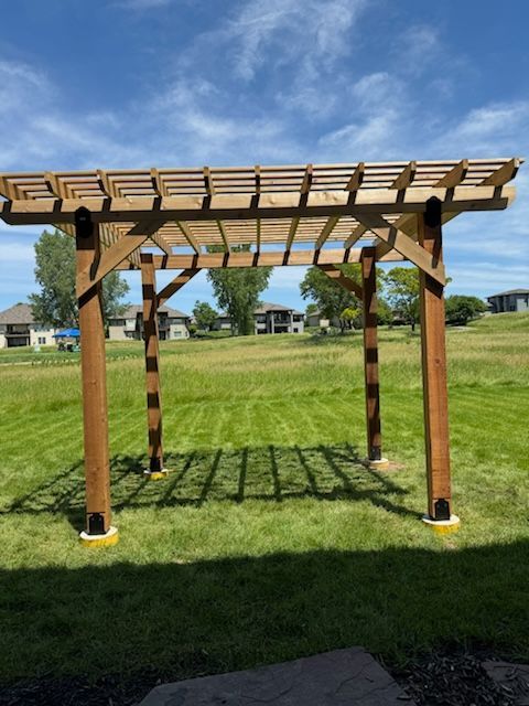 A wooden pergola is sitting in the middle of a lush green field.