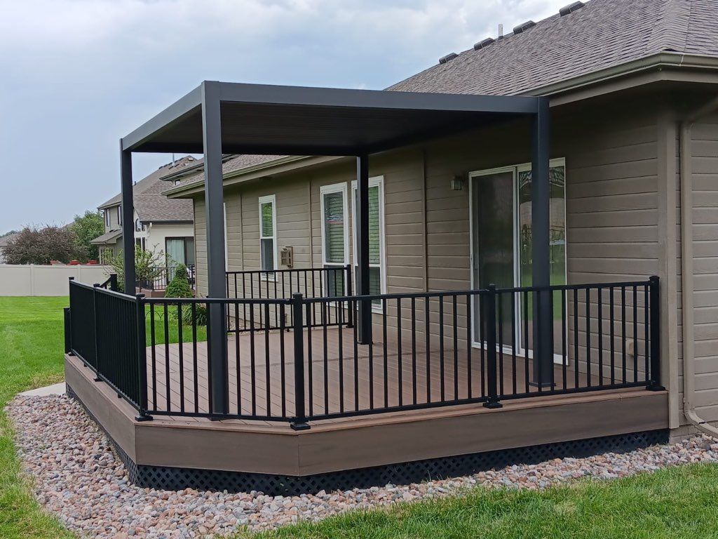 A deck with a pergola on top of it in front of a house.