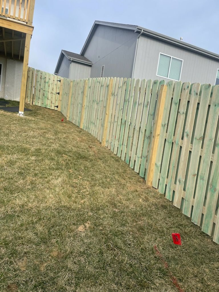 A wooden fence is sitting on top of a grassy hill next to a house.