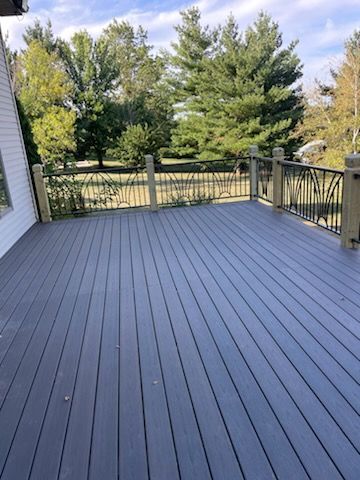 A large gray deck with a railing and trees in the background.