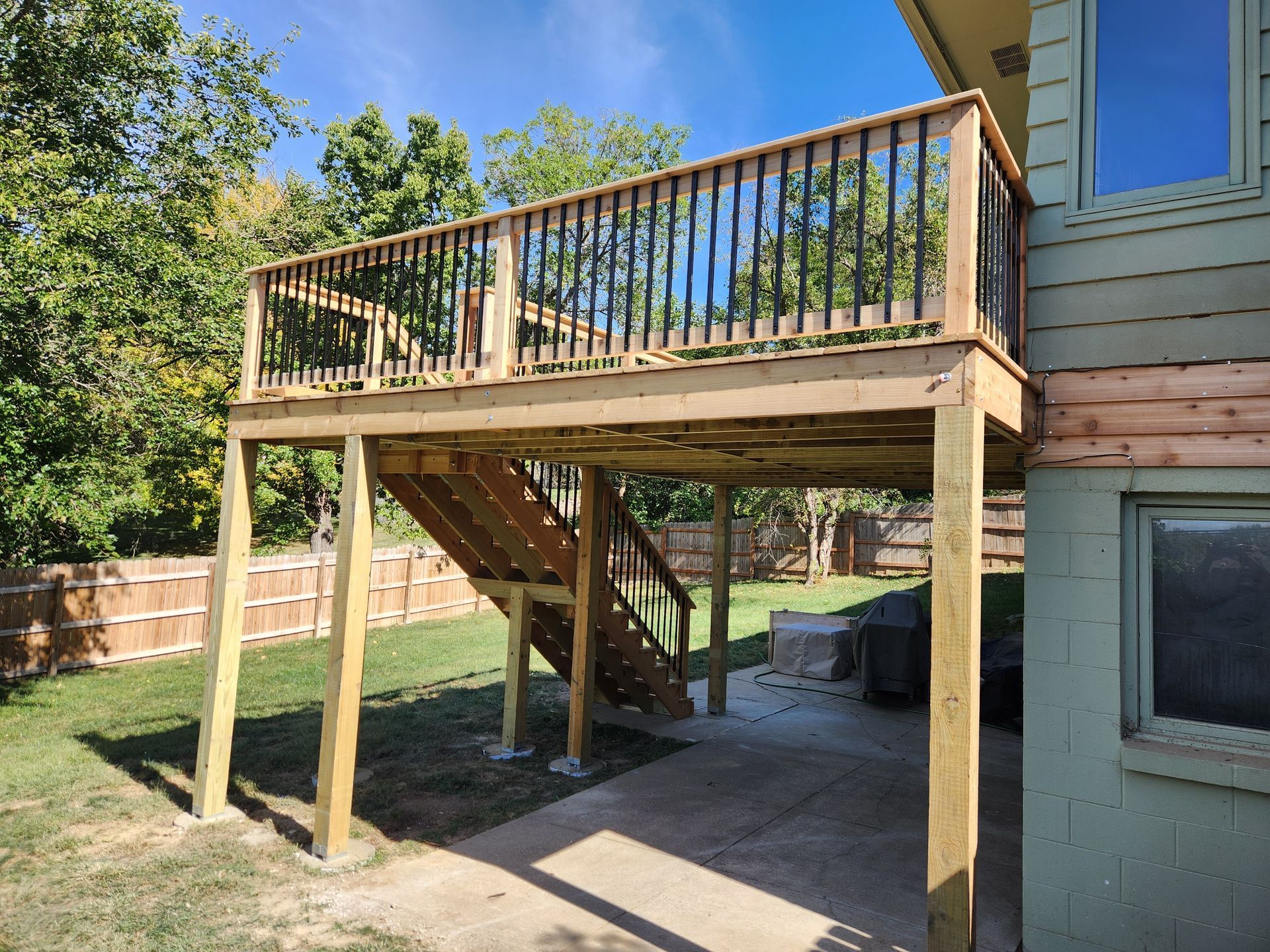 A wooden deck with stairs leading up to it is in the backyard of a house.