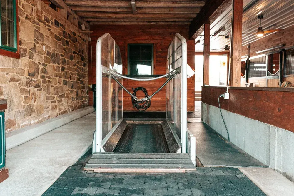 A horse wash station, with a metal and transparent enclosure, is in a barn setting.