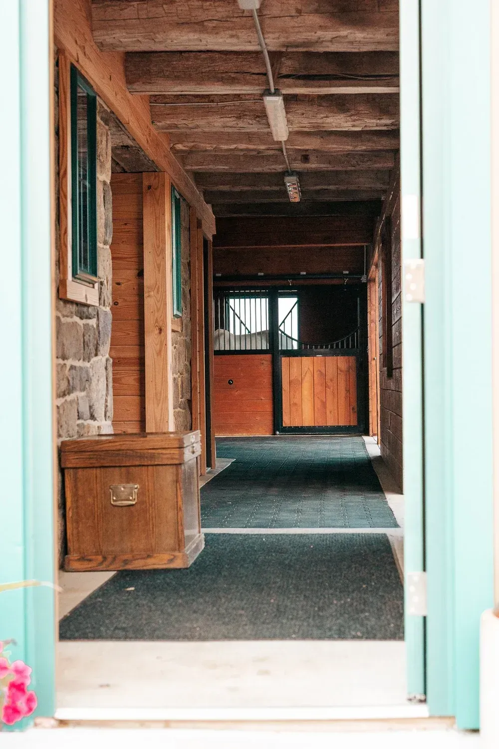 Horse stable interior: wood, stone walls, stalls with doors, turquoise trim, dark floor mat.