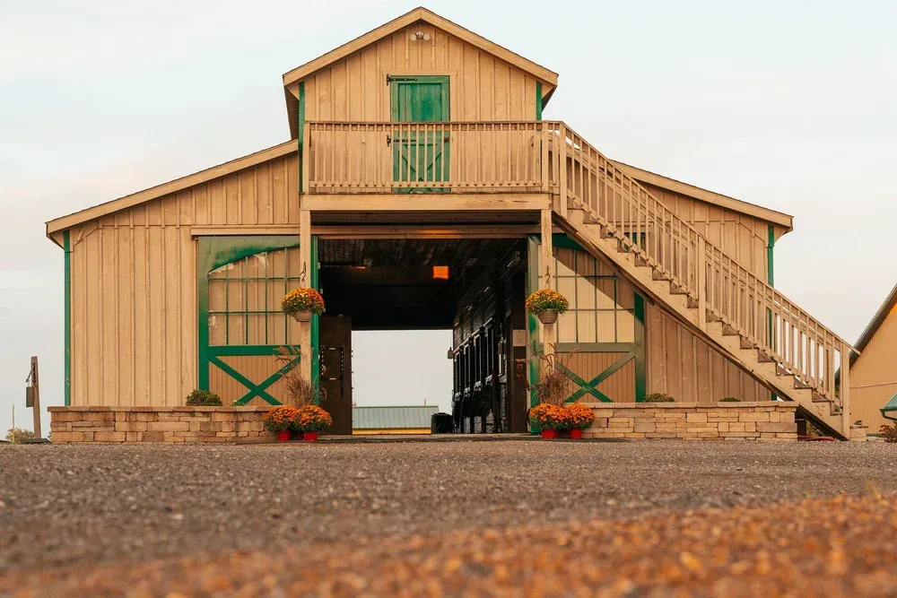 Wooden barn with green trim, open doorway, stairs, and flower pots.