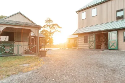 Barn complex with tan and green buildings; gravel drive, bright sunset.