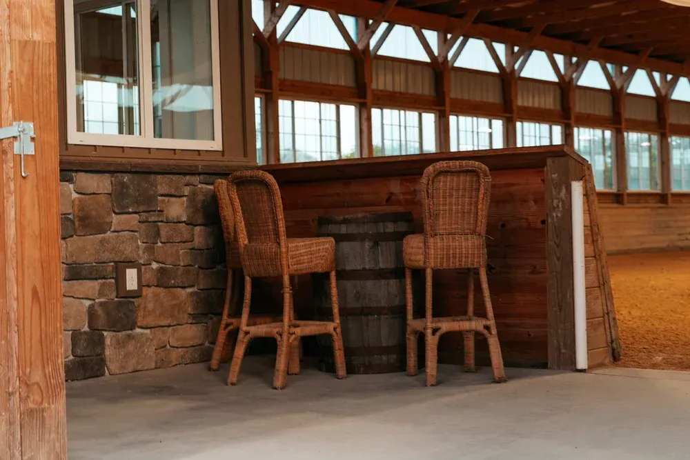 Two wicker bar stools and barrel bar under wooden beam ceiling.