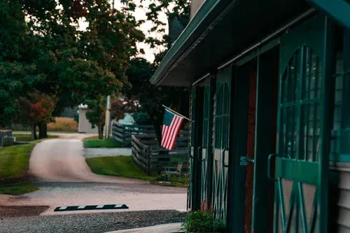 Barn doors with American flag, overlooking a paved road and surrounding trees.