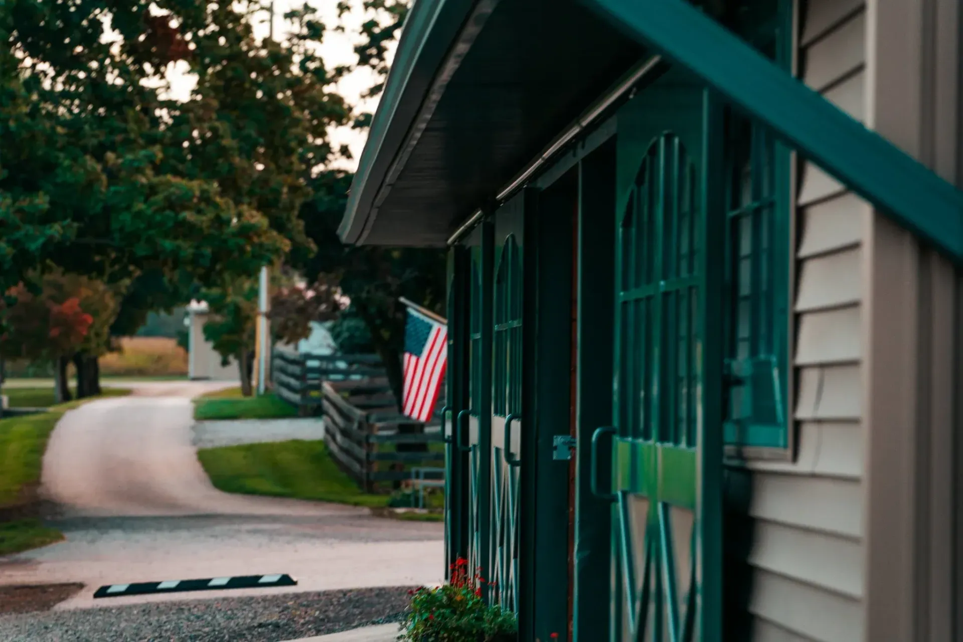 Barn with green doors and an American flag, overlooking a paved driveway.