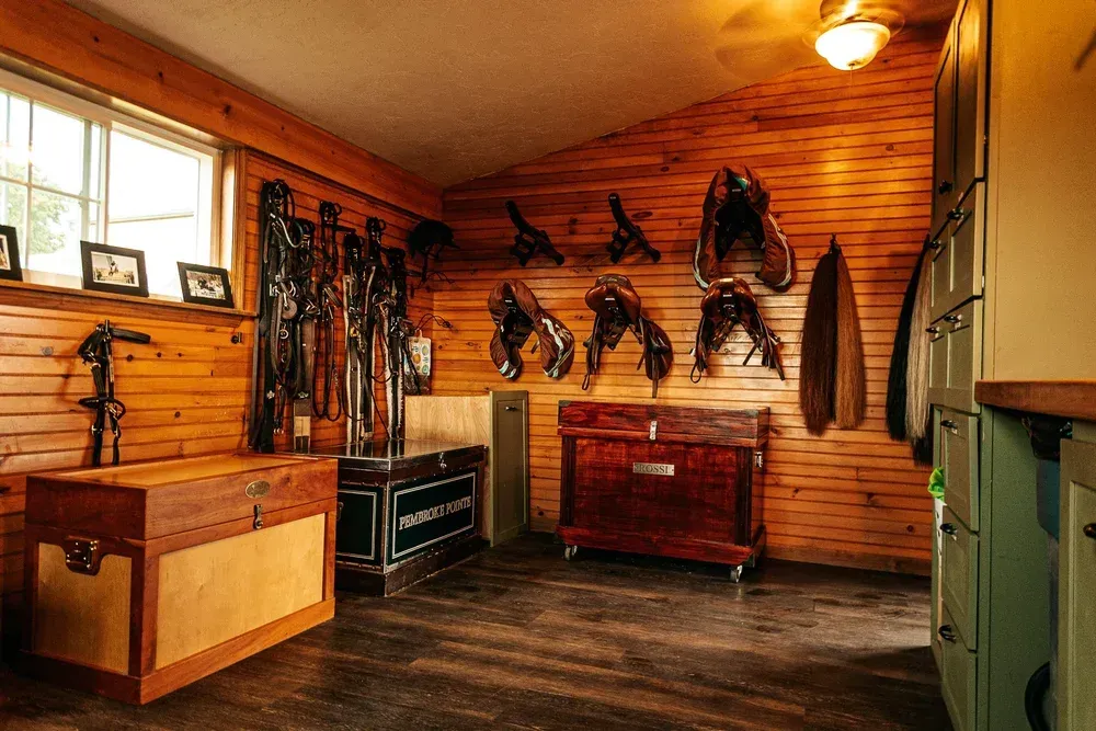 Equestrian tack room with wood paneling, saddles, bridles, and storage chests.