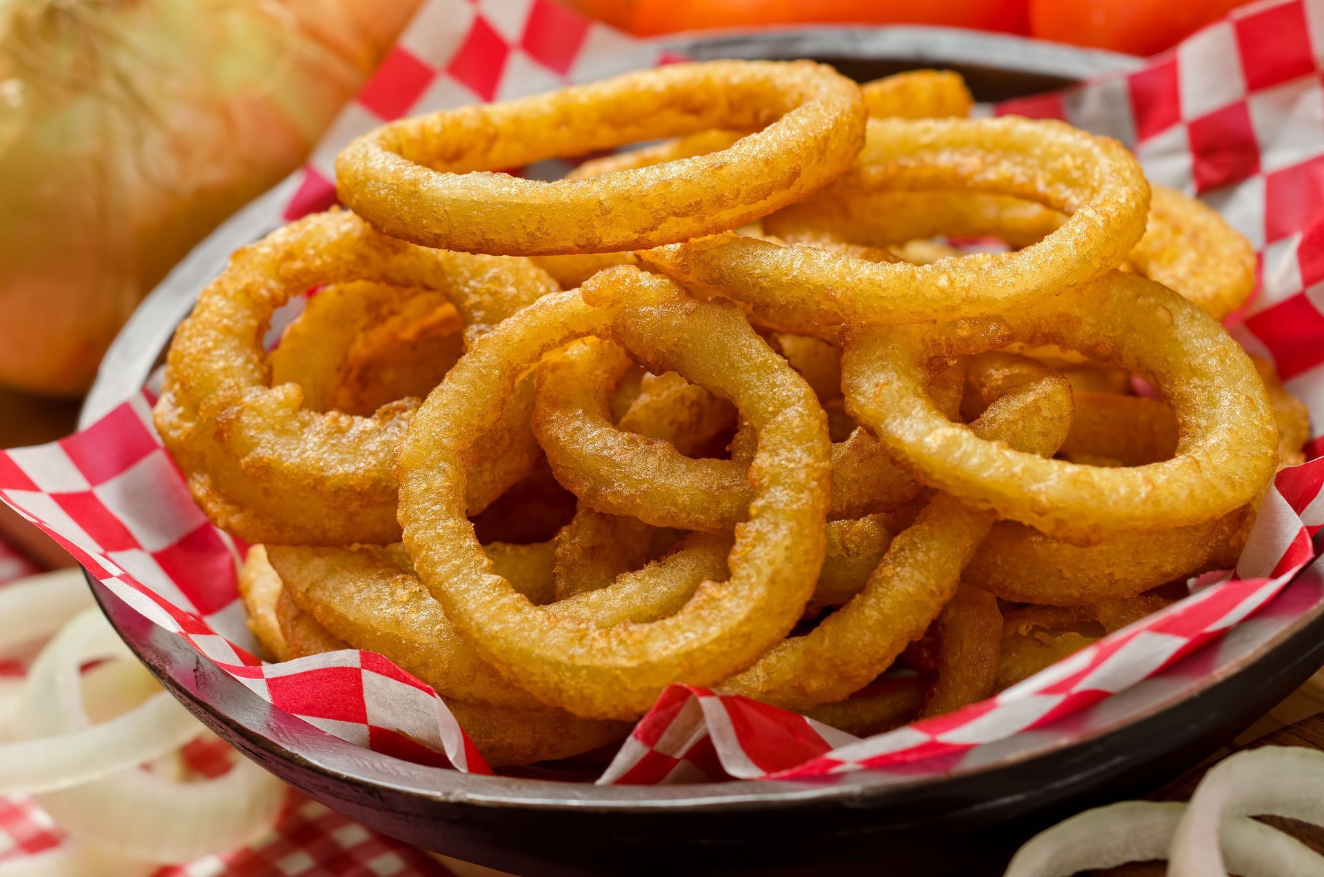 Golden-fried onion rings in a bowl, accompanied by red and white checkered paper.