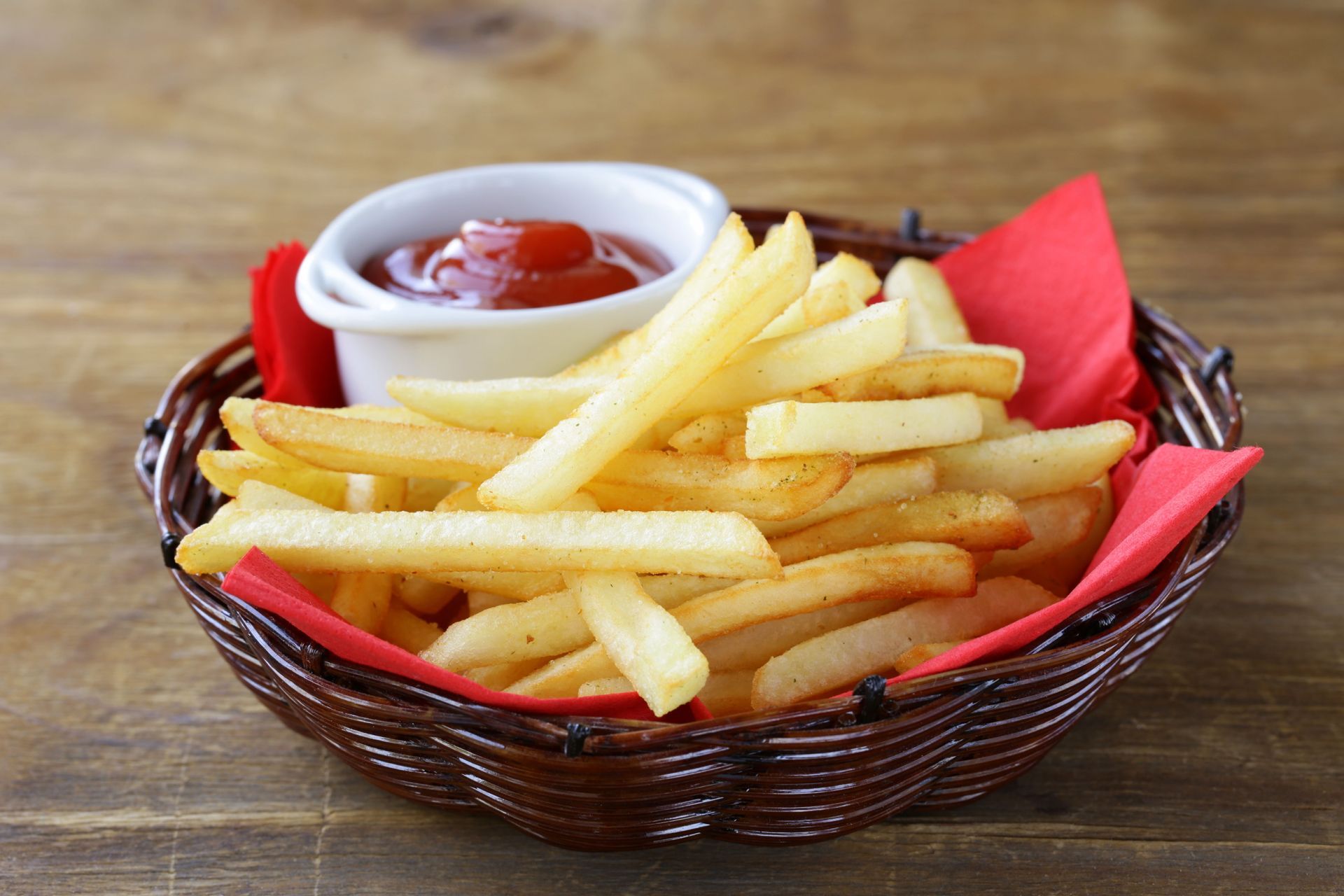 French fries in a basket with a small bowl of ketchup and a red napkin.