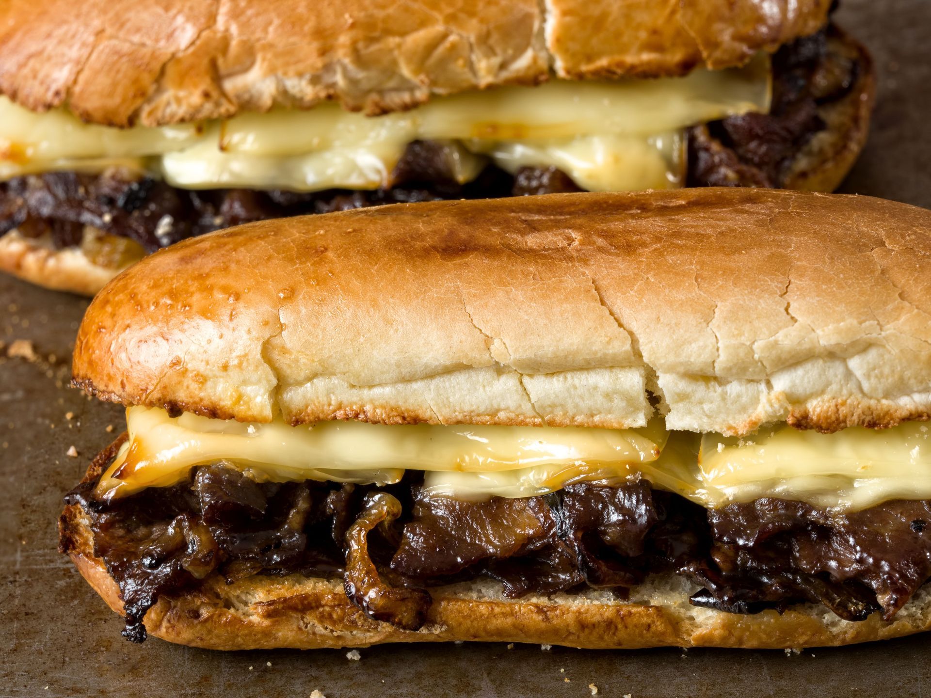 Two French dip sandwiches with melted cheese and caramelized onions.