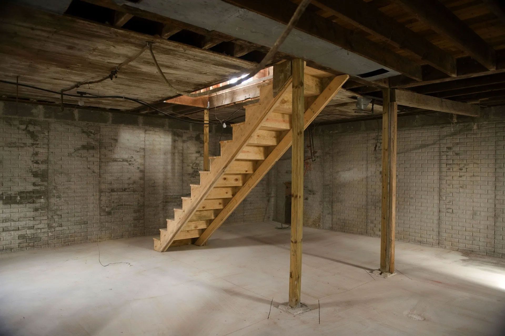 Wooden stairs in a unfinished basement, leading up to a hole in the ceiling.