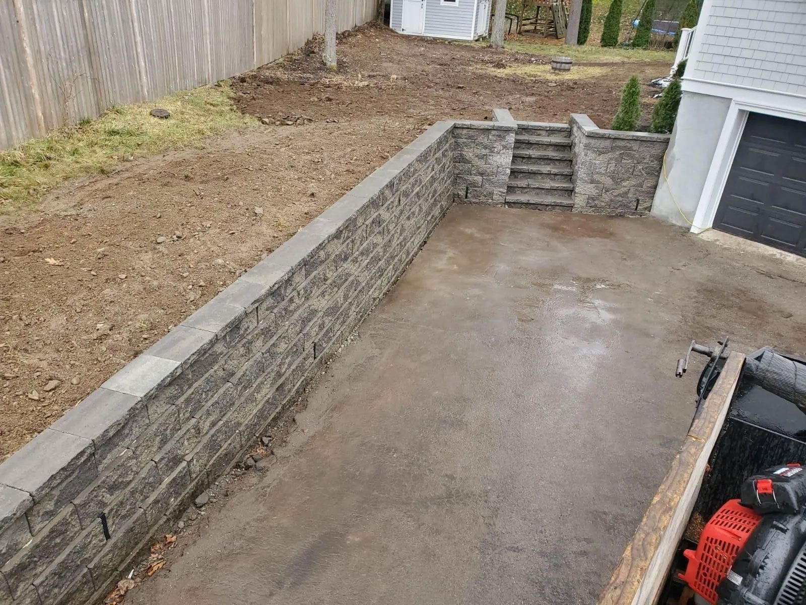 Stone retaining walls border a driveway with steps up to a yard. A garage is on the right.