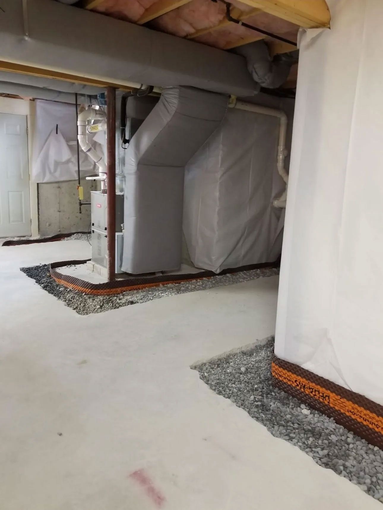 Basement with gravel perimeter drainage, concrete floor, mechanical equipment, and white wall covering.