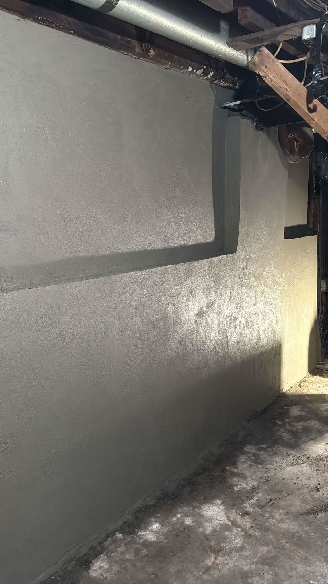 Gray stucco wall with shadow and wooden beams above.