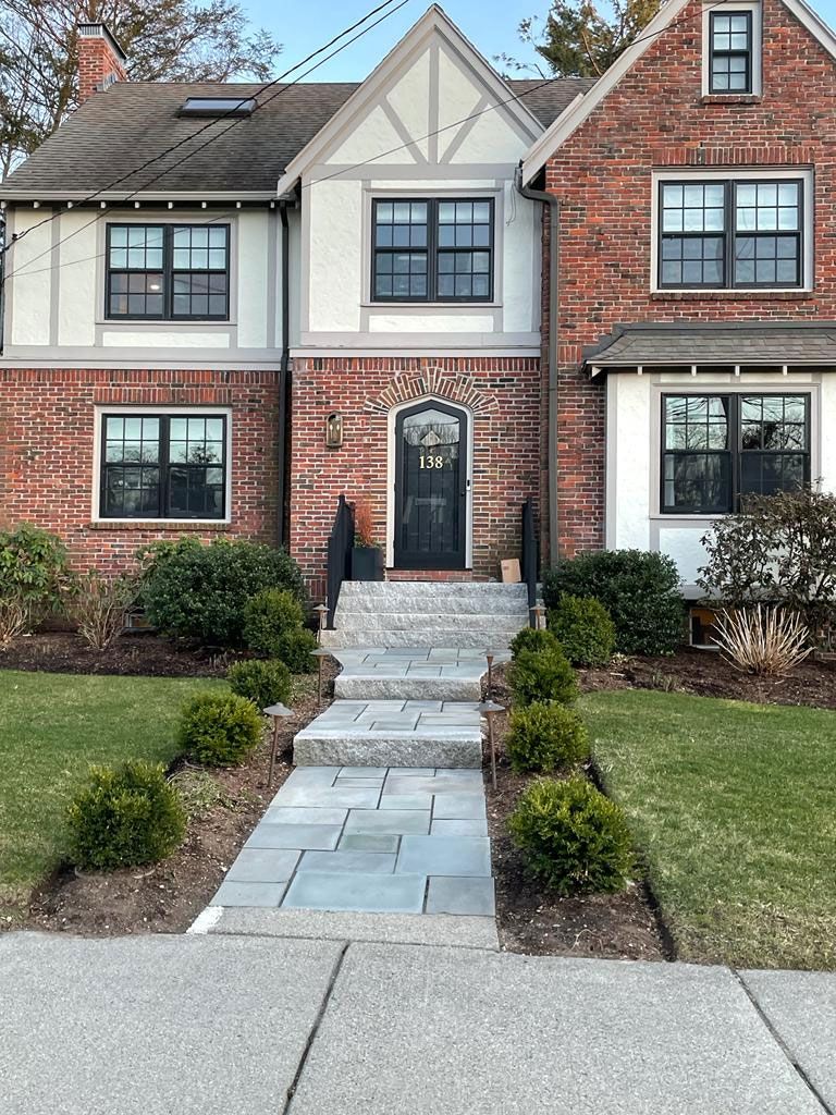 Brick Tudor-style house with a stone walkway leading to a black front door. Green bushes line the path.