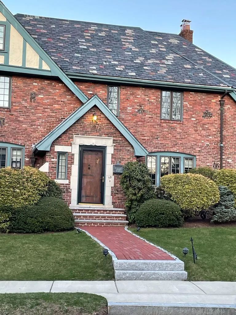 Red brick Tudor-style house with green trim, a dark roof, and a brick pathway.