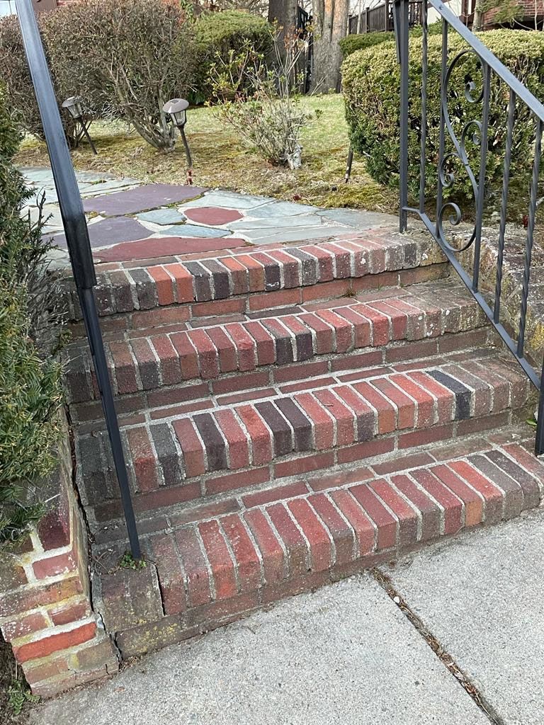 Brick steps leading up to a walkway. Metal railing on right. Brick and concrete construction.