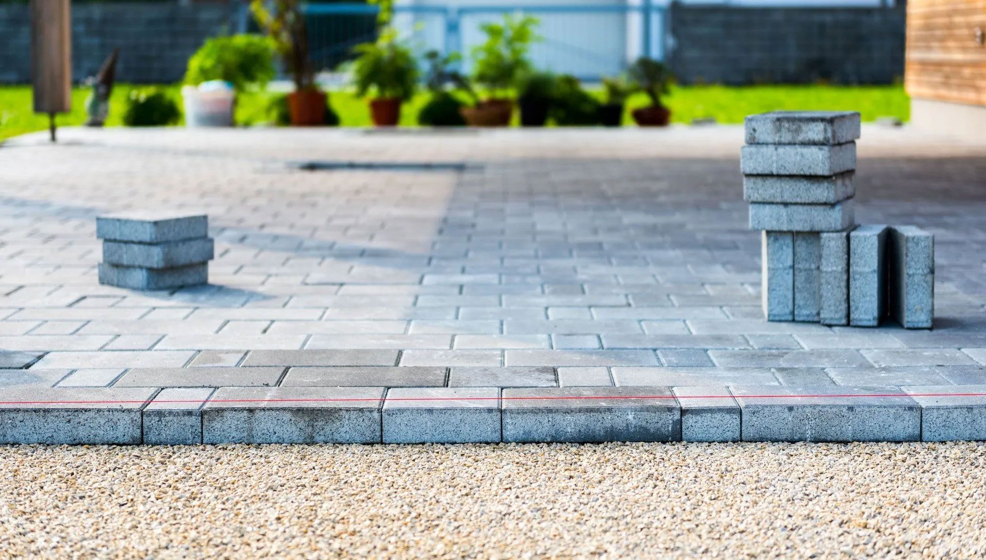 Patio under construction with stacked gray pavers, gravel, and landscaping in the background.