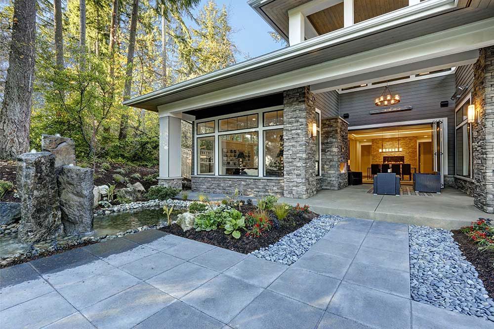 Modern house exterior with stone accents, a pond, and a paved patio.