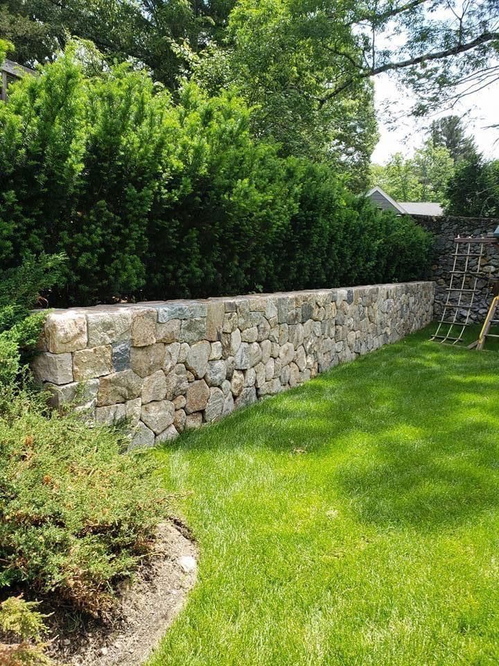 Stone wall with green lawn and bushes.