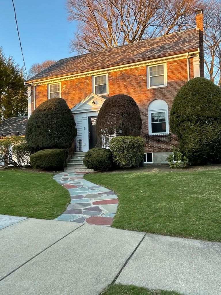 Brick house with colorful walkway, green lawn, and large trimmed bushes.