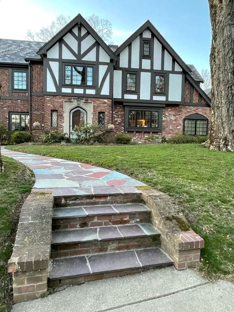 Brick Tudor-style house with a colorful pathway leading to the front door.