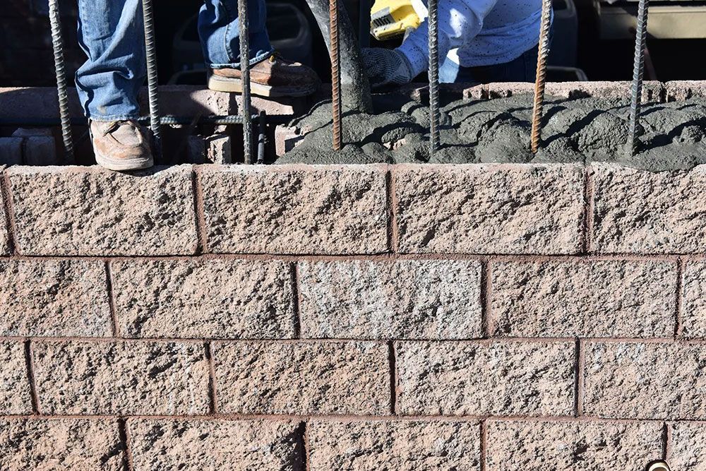 Construction of a retaining wall with brown textured blocks, concrete pouring, and rebar.