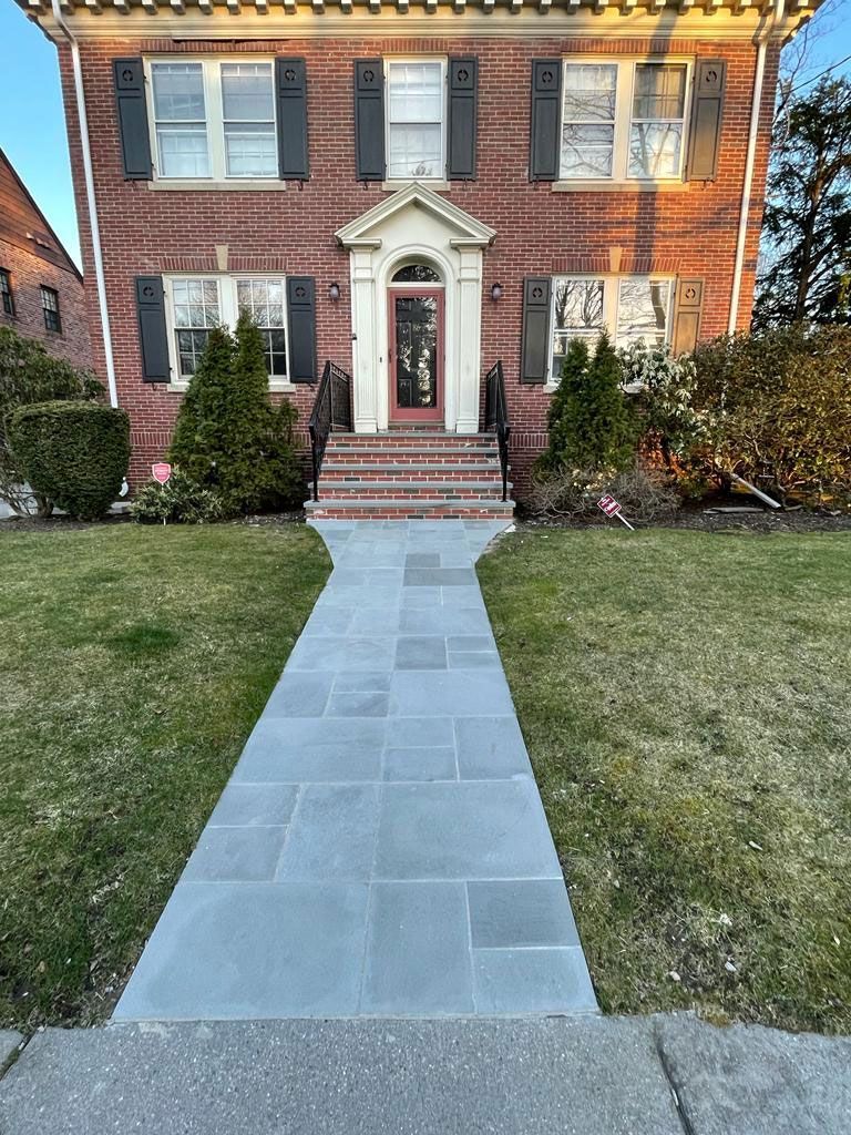 Brick house with blue stone walkway, green lawn, and shrubbery in front.