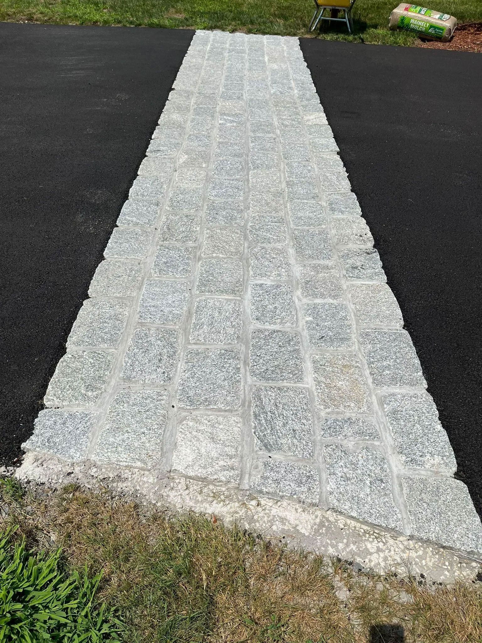 Stone paver pathway on asphalt, bordered by grass.