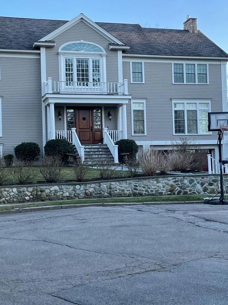 Two-story beige house with white trim, arched window, front porch, and a basketball hoop in the driveway.