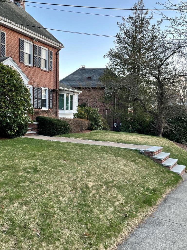 A brick house with shutters, lawn, and steps leading to a pathway on a sunny day.