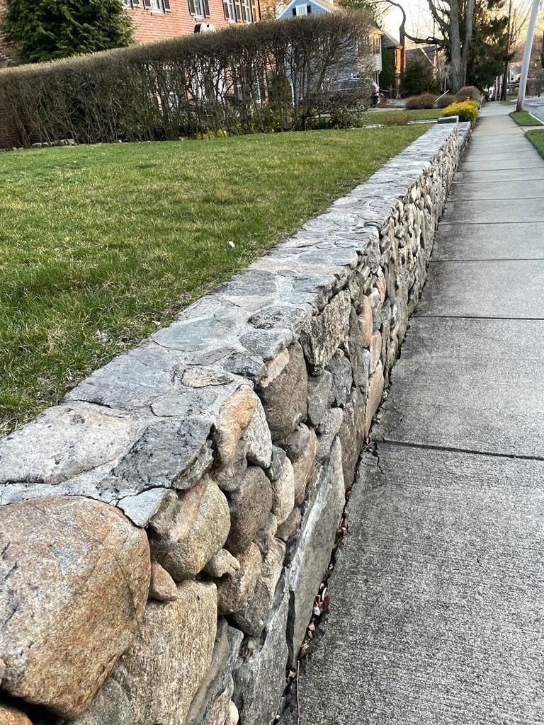 Stone wall borders sidewalk and lawn on a residential street.