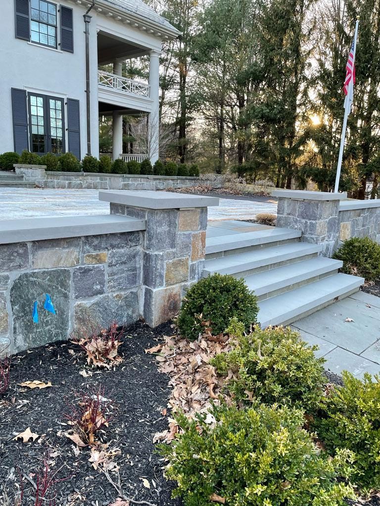 Stone steps leading up to a house, with a retaining wall and landscaping.