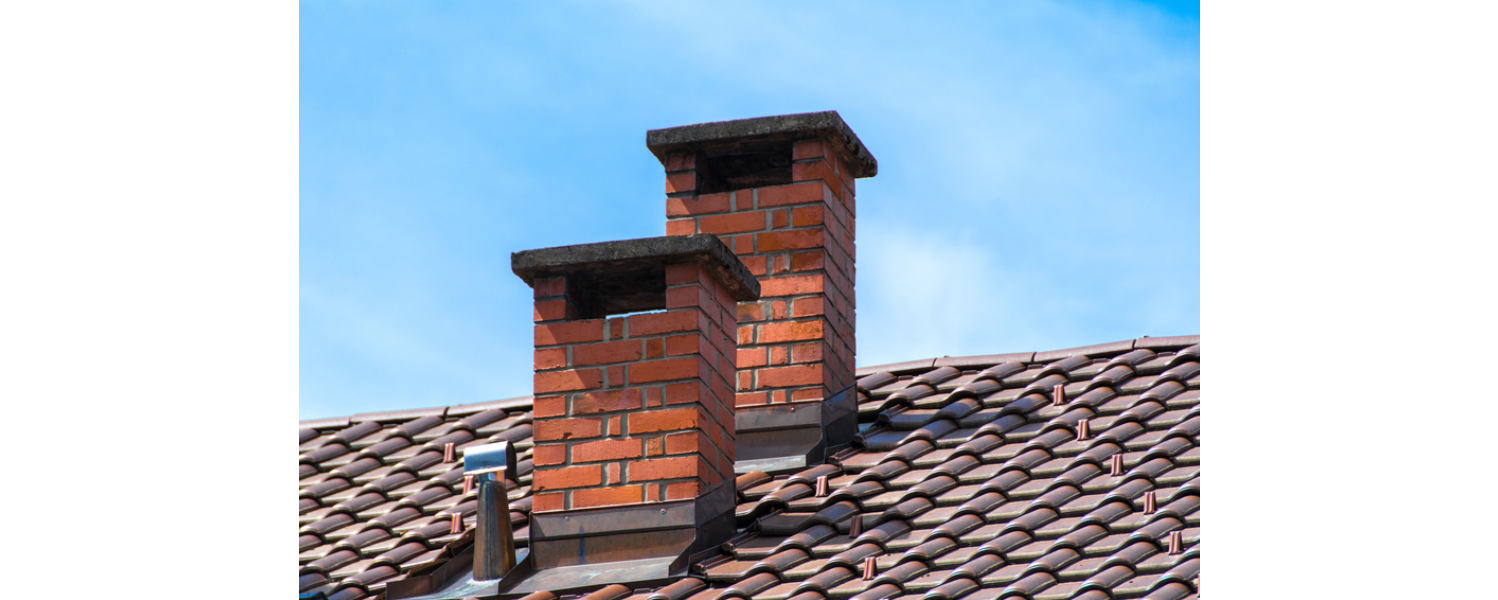 Two brick chimneys on a tile roof against a blue sky.