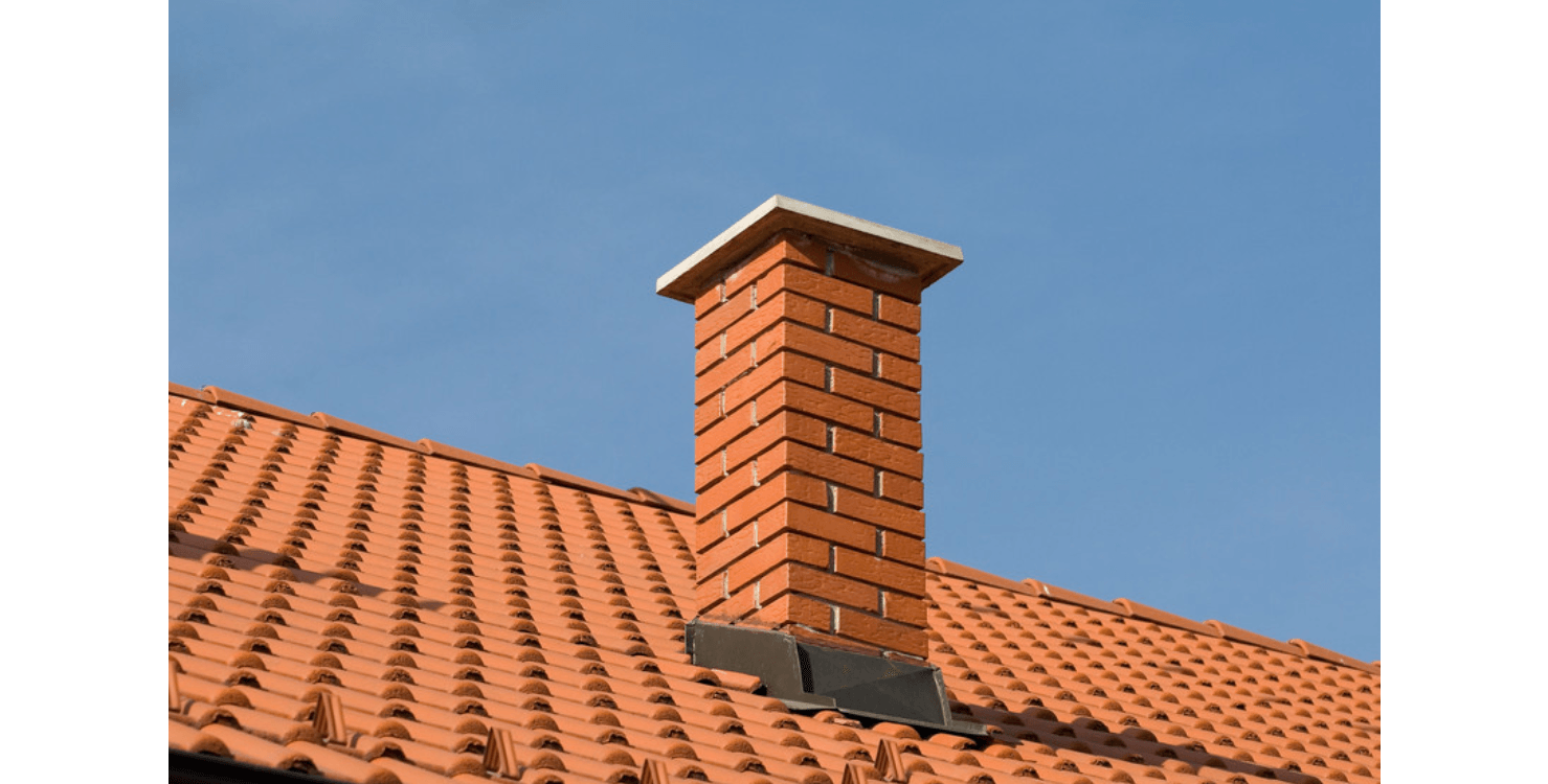 Brick chimney on a terracotta-tiled roof against a clear blue sky.