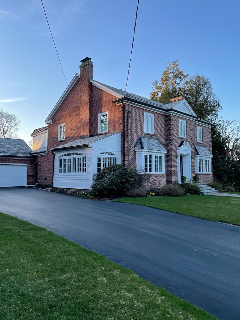 Brick house with a long driveway and green lawn under a blue sky.