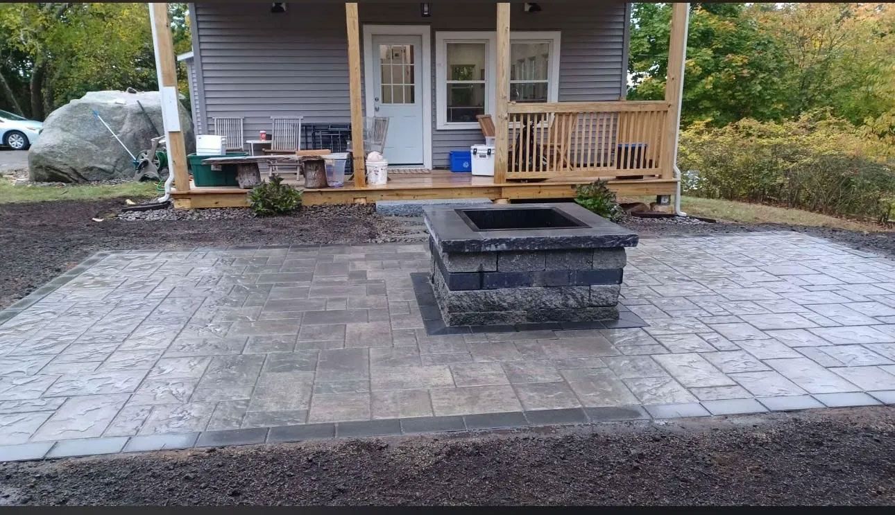 Fire pit on a paver patio in front of a small house with a porch.